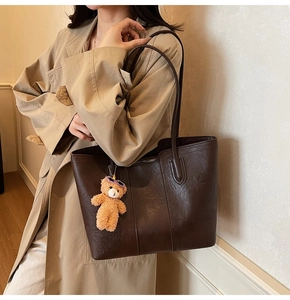 Detail of dark brown faux leather tote bag with cute plush bear charm on shoulder strap