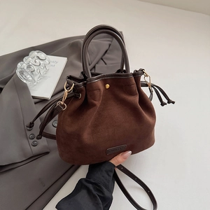Detailed view of dark brown suede bucket bag with drawstring closure and golden hardware