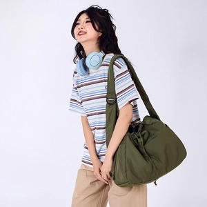 Detail of olive green nylon drawstring bag featuring wide shoulder strap and matte metal buckles