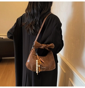 Détail du sac d'épaule en daim marron avec nœud en cuir et pompon en perles de bois naturel