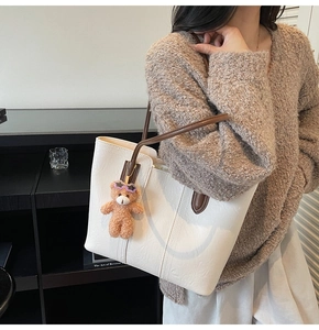 Detail of off-white tote bag featuring brown straps and a cute plush bear pendant