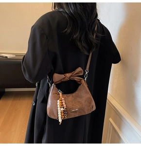 Détail du sac en daim marron avec poignée à nœud et pompon à perles bohème
