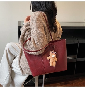 Detail of burgundy tote bag on model showing large capacity and bear charm accessory