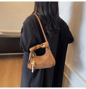 Détail du sac bandoulière en daim marron avec nœud en cuir et breloque à pompon perlé