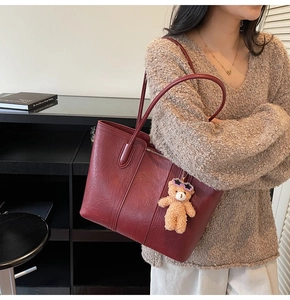 Detail view of burgundy leather tote bag with plush bear pendant and long shoulder straps