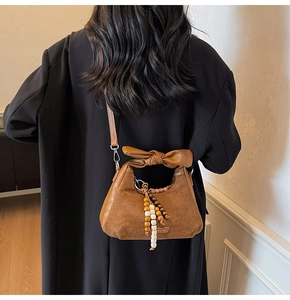Détail d'un sac en cuir mat marron caramel avec poignée nœud élégante et pompon décoratif