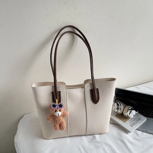 Detail of cream tote bag with wrinkled texture, brown handles, and a cute bear charm