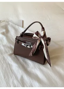 Detail of dark brown litchi grain leather bag with silver metal lock and silk scarf