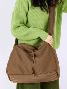 Brown large capacity nylon drawstring crossbody bag styled on a green knit sweater