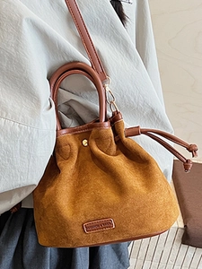 Brown suede bucket bag with leather trim and drawstring, shown in a lifestyle setting