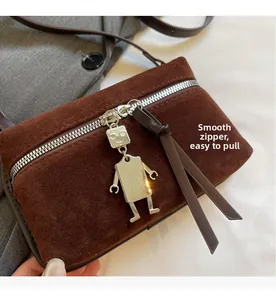 Détail du sac à bandoulière en daim marron avec fermeture éclair et pendentif robot