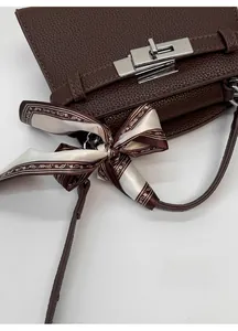Detail of dark brown litchi grain leather bag with silver metal lock and silk scarf