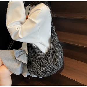 Detailed view of checkered drawstring shoulder bag worn by model on wooden stairs