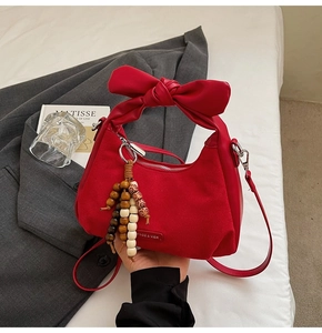 Détail du sac rouge en daim avec une grande anse à nœud et un gland décoratif