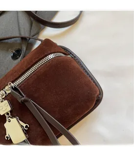 Detail of brown suede crossbody bag with metallic robot charm and silver zipper accents