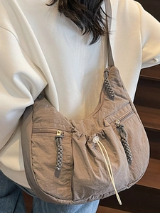Chic crescent-shaped taupe nylon shoulder bag with functional zippers and woven charms