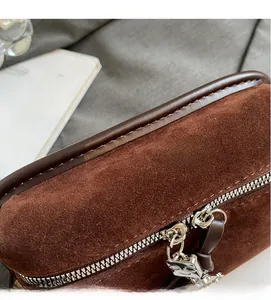Detailed close-up of dark brown suede fabric and silver metal zipper on a square bag
