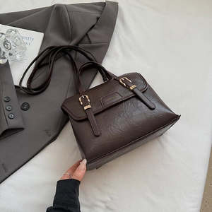 Close-up of vintage brown leather satchel with gold buckles and brand logo plaque