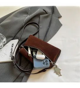 Détail du sac bandoulière en daim marron montrant l'espace pour téléphone et parfum