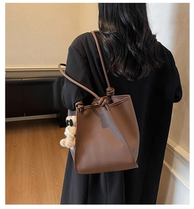 Detail of dark brown lychee leather tote bag featuring a cute teddy bear charm on shoulder strap