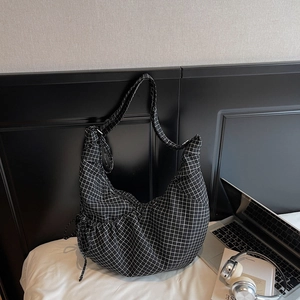 Minimalist black and white plaid hobo bag displayed with a laptop and headphones