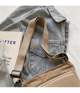 Detail of khaki nylon crossbody bag with wide woven strap and front zipper on denim jacket