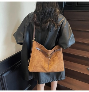 Detail of a large brown suede tote bag carried by a model against dark stairs