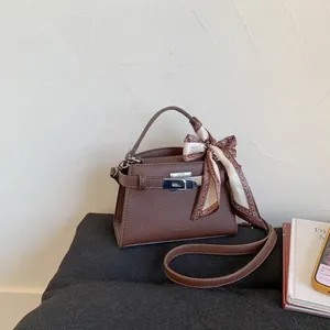 Close-up of brown litchi pattern leather handbag with silver lock and silk scarf on handle
