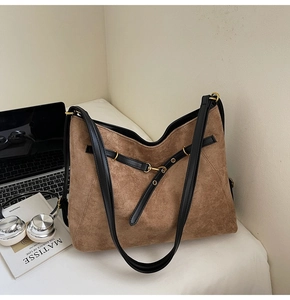 Brown suede tote bag detail with black leather straps and metal rings in a lifestyle setup
