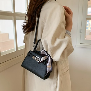Detail of black pebbled leather crossbody bag with silver twist lock and scarf wrapped handle