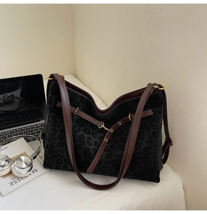 Detail of black leopard print tote bag with brown leather straps and gold metal buckle