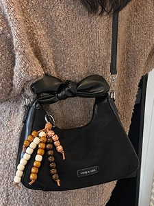 Sac demi-lune noir chic avec poignée en nœud et pompon perlé sur un pull en maille