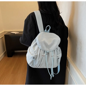 Vista detallada de una mochila minimalista de nailon azul con cordón y solapa frontal
