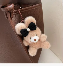 Detail of light brown plush teddy bear charm with black bow tie on textured leather bag