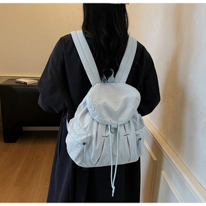 Detalle de la mochila de nailon azul claro con cierre de cordón y correas acolchadas
