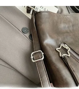 Detail of a brown leather shoulder bag with a star-shaped zipper pull on a grey suit