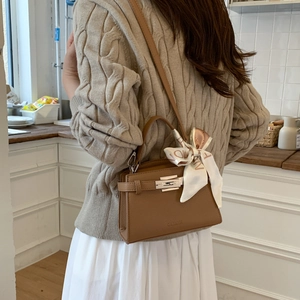 Detail of caramel brown pebbled leather handbag with silver lock and silk scarf on handle