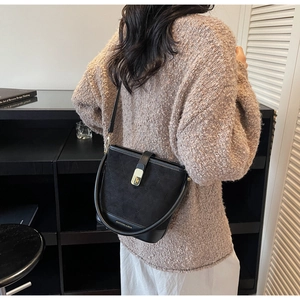 Detail of black suede bucket bag showing contrast texture and gold hardware lock