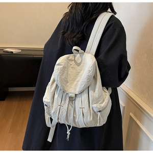 Detalle de la mochila de nailon crema con cierre de cordón y bolsillo lateral cremallera