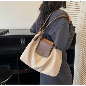 Detail of large canvas tote bag with brown leather flap and slim shoulder strap