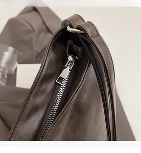 Close-up of smooth silver metal zipper and stitching on dark brown leather tote bag