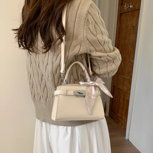Detail of beige lychee leather crossbody bag with silver lock and silk scarf on handle