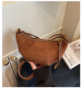 Dettaglio borsa a mezzaluna in camoscio marrone con tracolla intrecciata e anelli d'oro