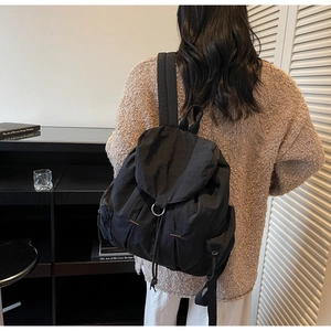 Vista trasera de modelo con mochila de nailon negro con hebilla metálica y cordón