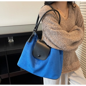Detail of royal blue suede tote bag featuring black leather flap and round snap closure