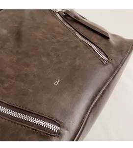 Detailed close-up of dark brown vintage faux leather texture and metallic zipper on tote bag