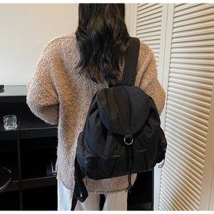 Detalle de la mochila de nailon negro con cierre de cordón y anillo metálico en la solapa