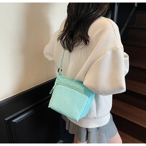 Detail showing mint green nylon crossbody bag with front zipper pocket and adjustable strap
