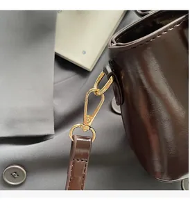 Close-up of glossy brown leather shoulder bag with shiny gold metal hardware detail