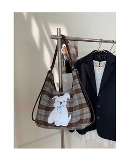 Detail of plaid tote bag featuring white puppy embroidery with blue bow and brown leather strap